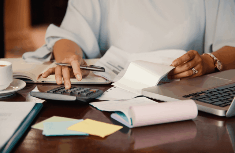 Imagem de uma pessoa trabalhando em uma mesa desorganizada com documentos, calculadora, laptop e caneta, focada em regularizar as obrigações acessórias da Reforma Tributária.